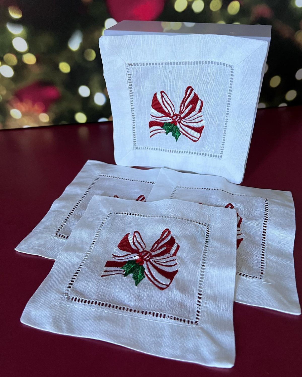 White cocktail napkins with embroidered red striped bows on a red surface.