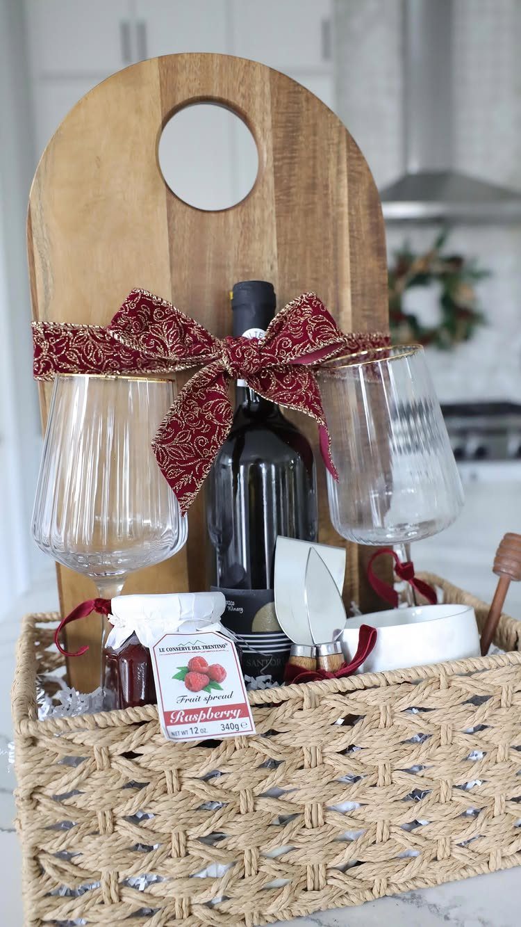 Woven gift basket with wooden cheese board, wine bottle, glasses, and jam.