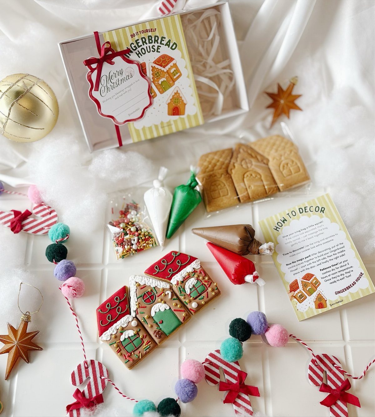 Gingerbread house kit with pre-baked pieces, icing, sprinkles, and a finished decorated house.