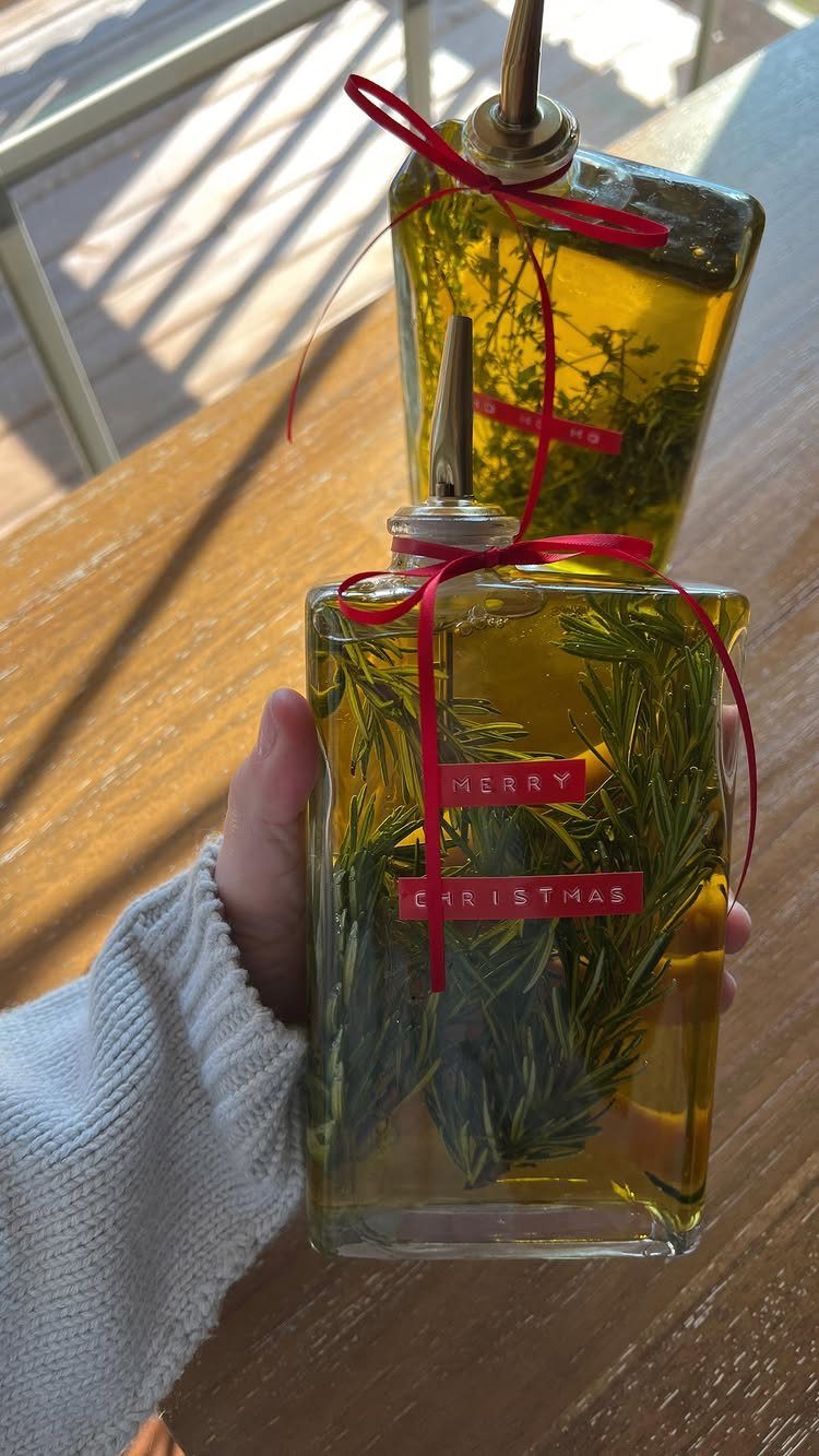 Two square glass bottles of rosemary infused olive oil with red Christmas ribbons.