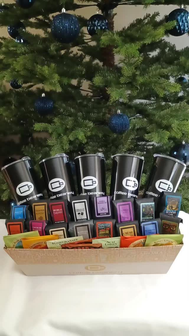 Coffee sampler gift basket with black canisters and colorful packets before a Christmas tree.