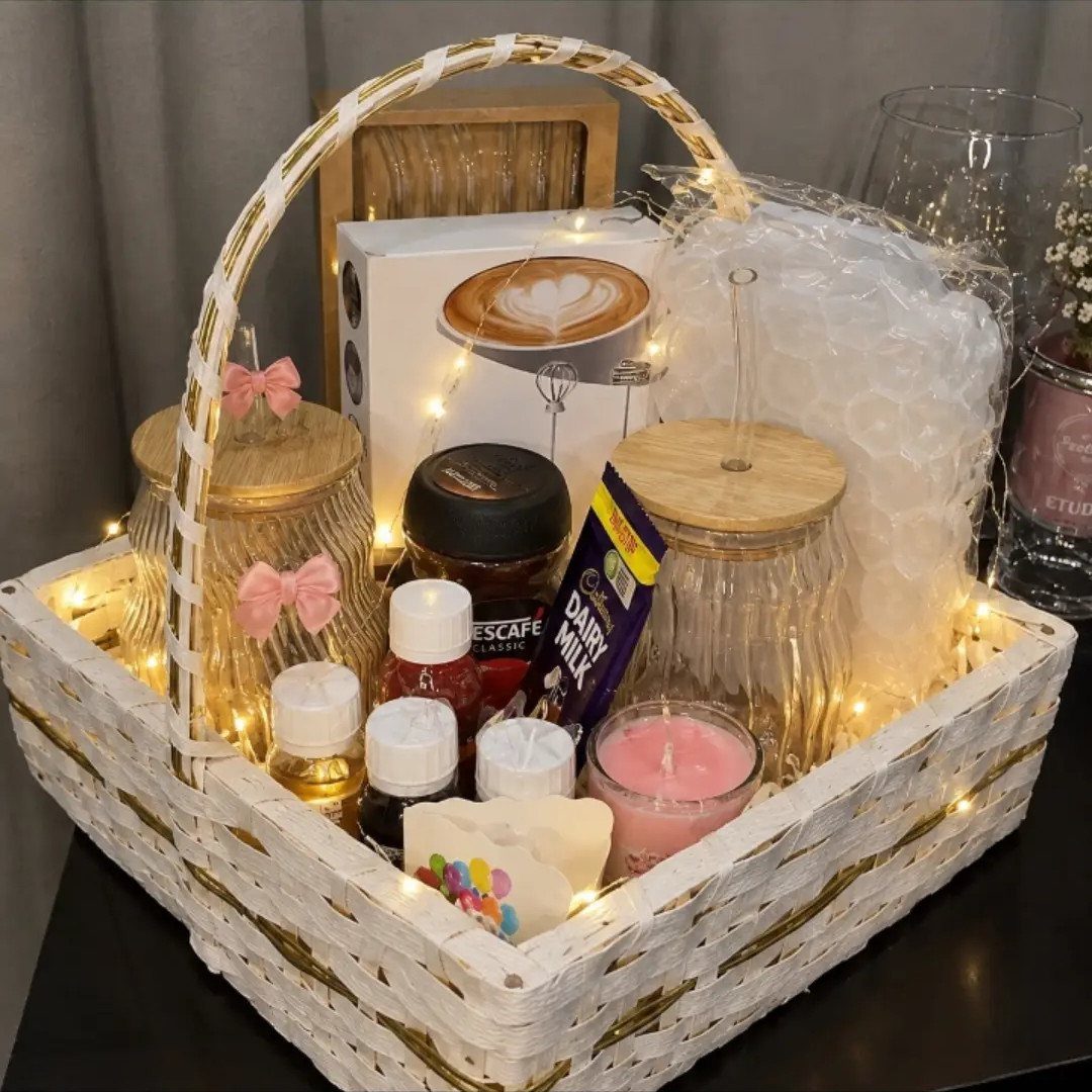 White wicker gift basket filled with coffee products, chocolates, and candles with fairy lights.