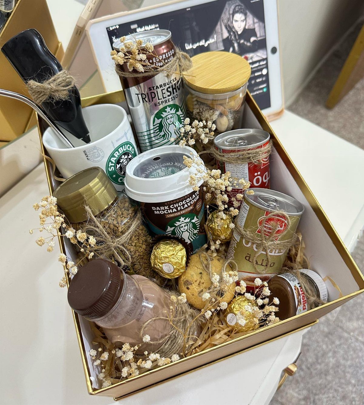 Coffee gift box with Starbucks mug, canned espresso, chocolates, and white flowers.