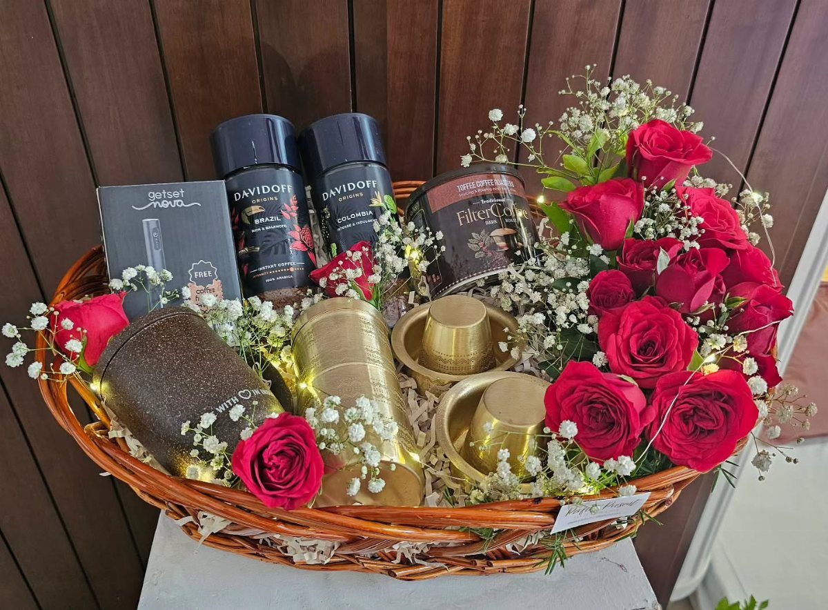 Wicker gift basket with gourmet coffee jars, gold canisters, and red roses.