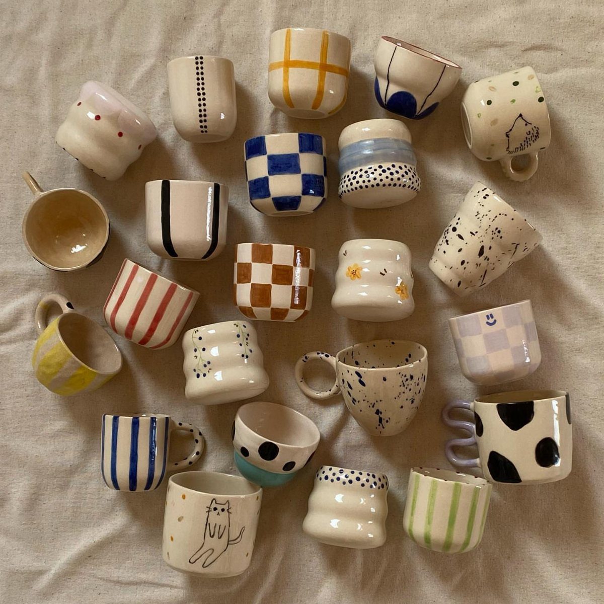 Assorted hand-crafted ceramic mugs with colorful patterns on a light fabric background