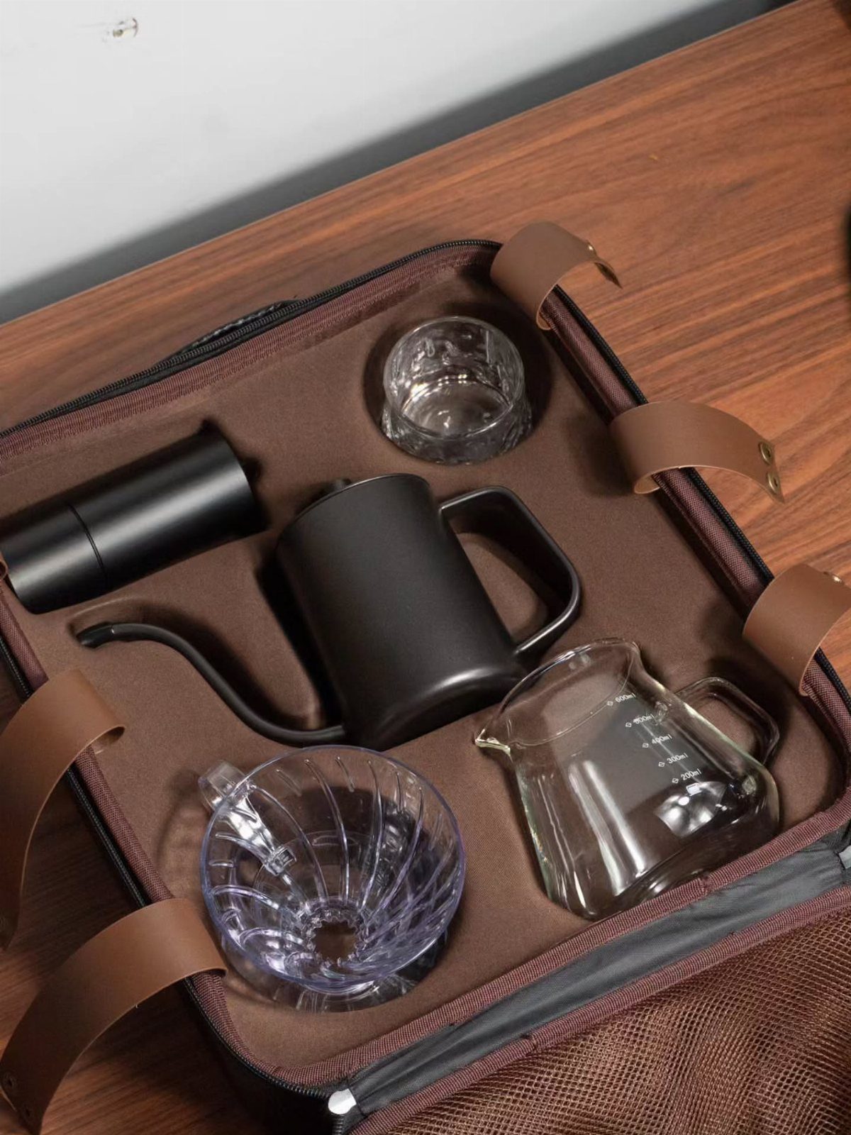 Coffee brewing kit with kettle, grinder, and glass server in a brown case.