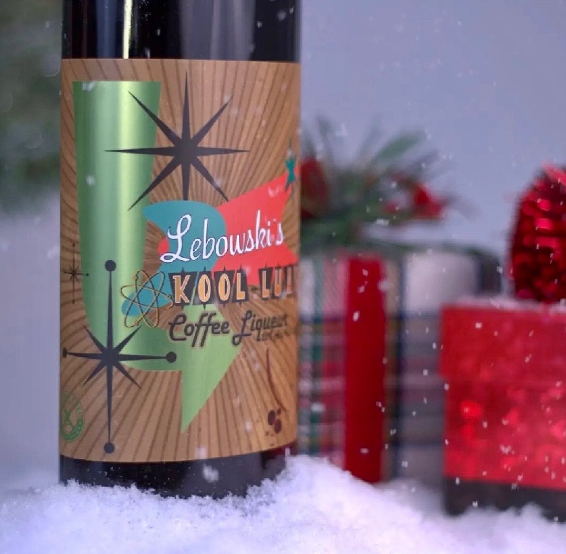 Bottle of coffee liqueur sitting in snow with festive gift boxes in background