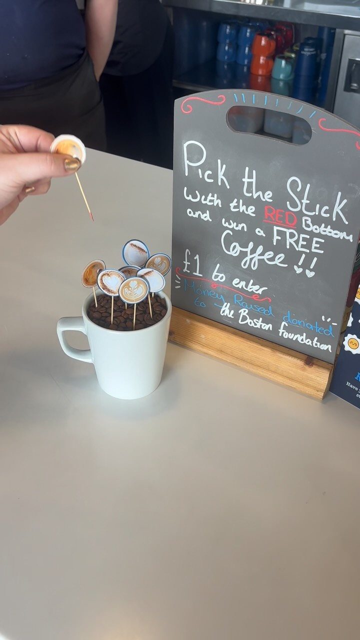 Hand picking a coffee-topped stick from a mug next to a game sign