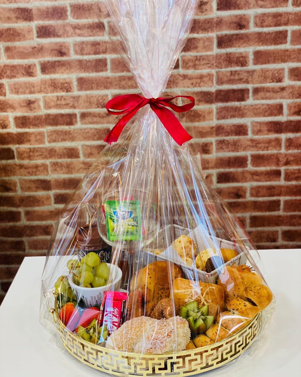 Gift basket with breads, grapes, and kiwi wrapped in cellophane with red bow.