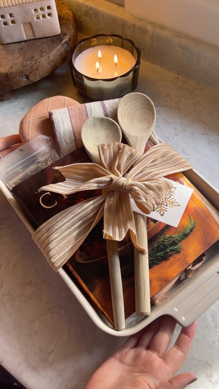 Cooking gift basket in a white tray with wooden spoons, cookbook, and ribbon.