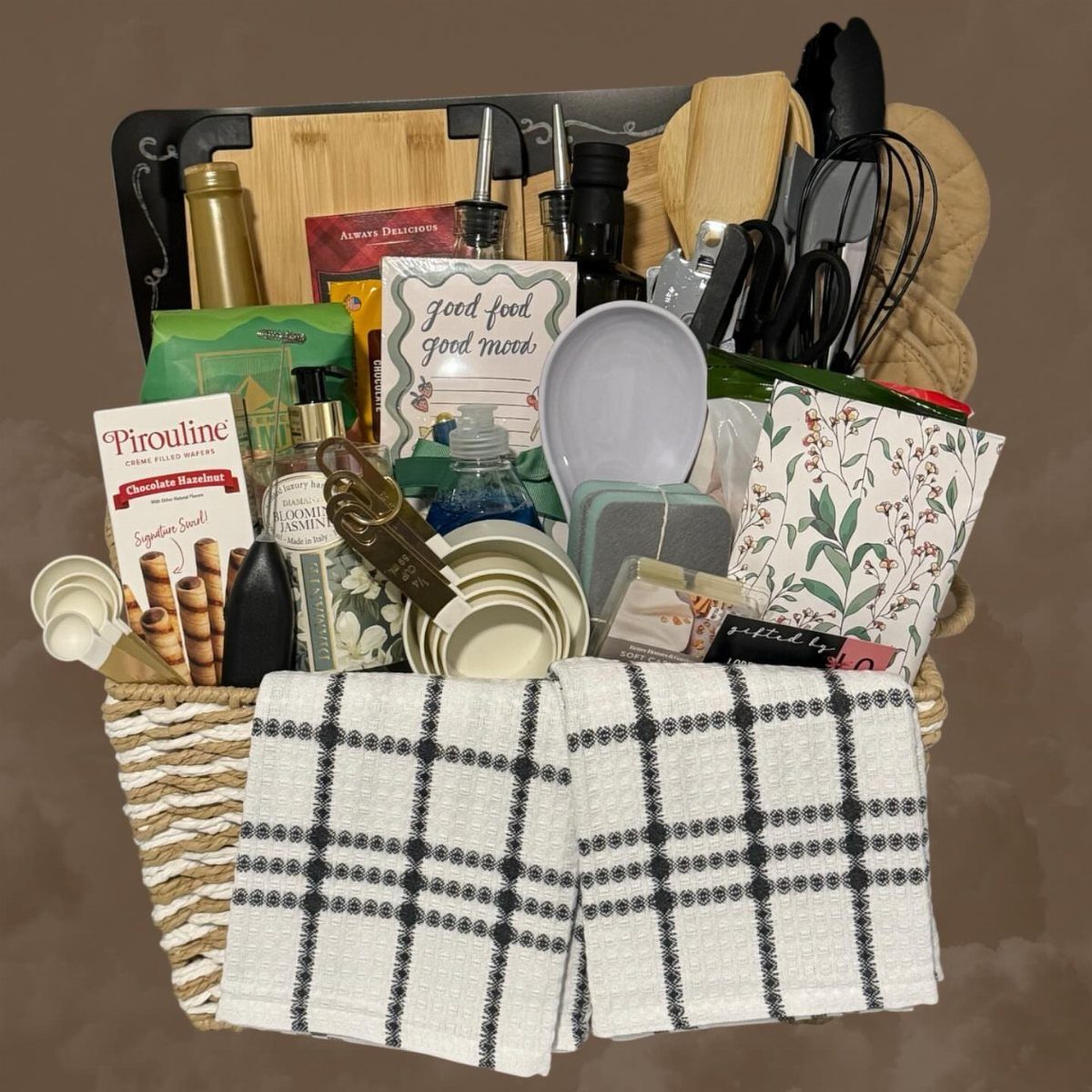 Woven gift basket filled with kitchen tools, snacks, and checkered dish towels.