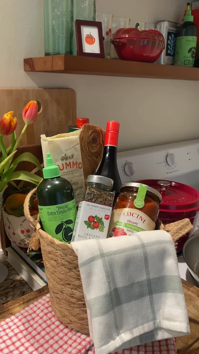 Woven gift basket filled with olive oil, pasta sauce, spices, and a kitchen towel.