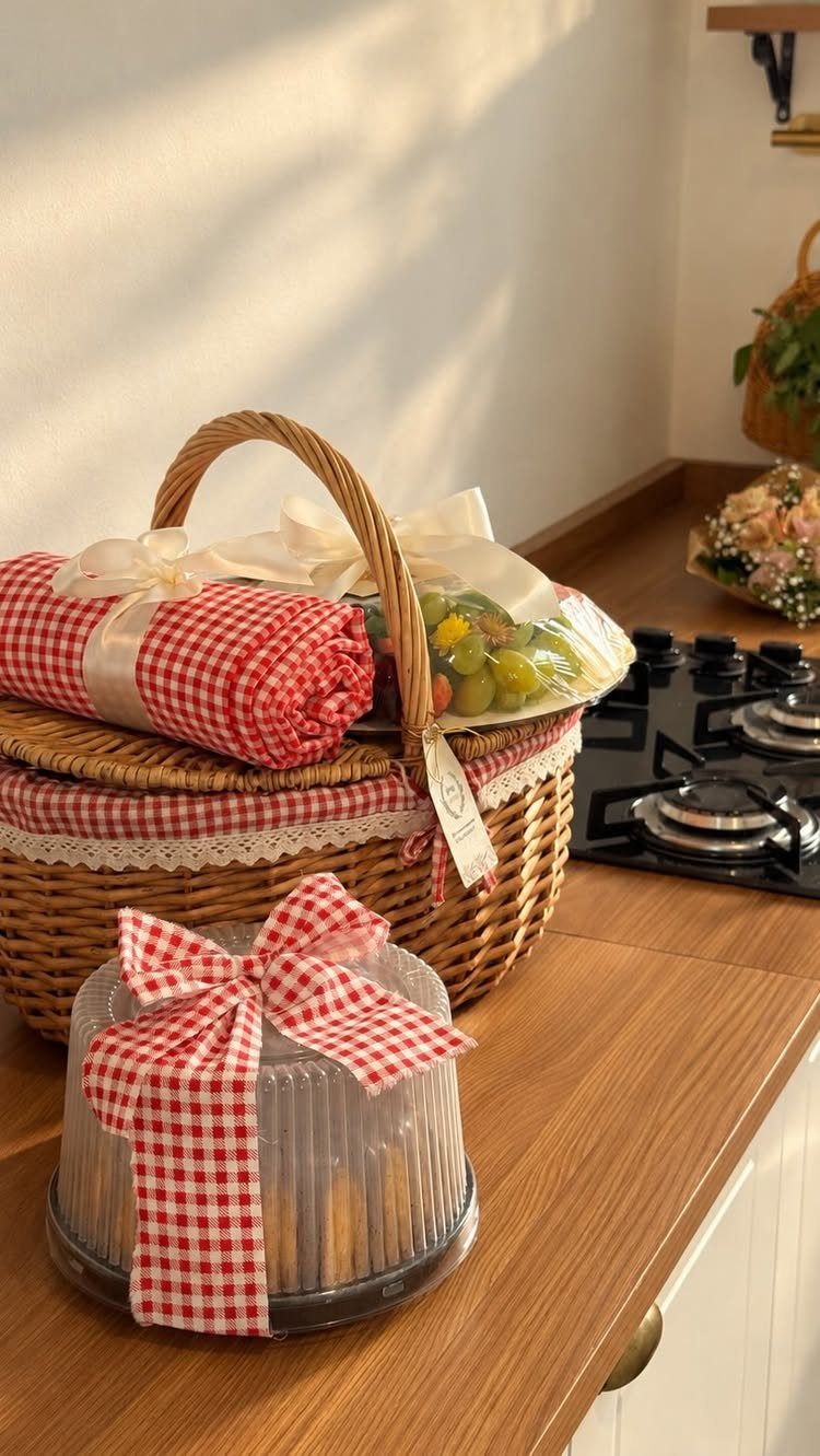 Wicker picnic basket with red checkered cloth and snacks on a wooden counter.