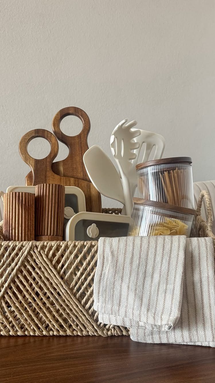 Woven wicker basket filled with wooden kitchen tools, utensils, and a linen cloth.