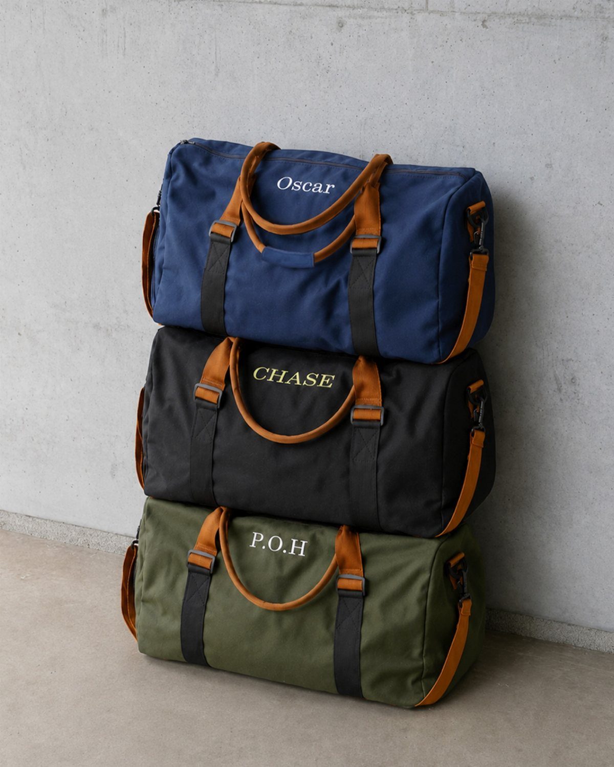 21 Cool Gifts for Adults: Practical Picks for 2026 5 Three personalized canvas travel duffle bags in blue, black, and green stacked vertically.