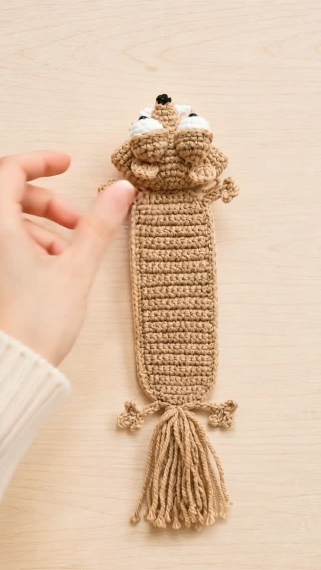 Tan crochet fox bookmark with a tassel held by a hand on wood.