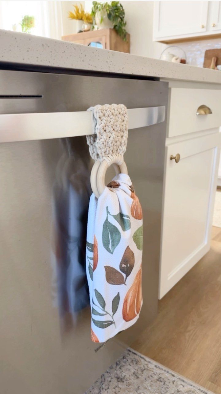 Beige crochet towel holder hanging on a dishwasher handle with a patterned towel.
