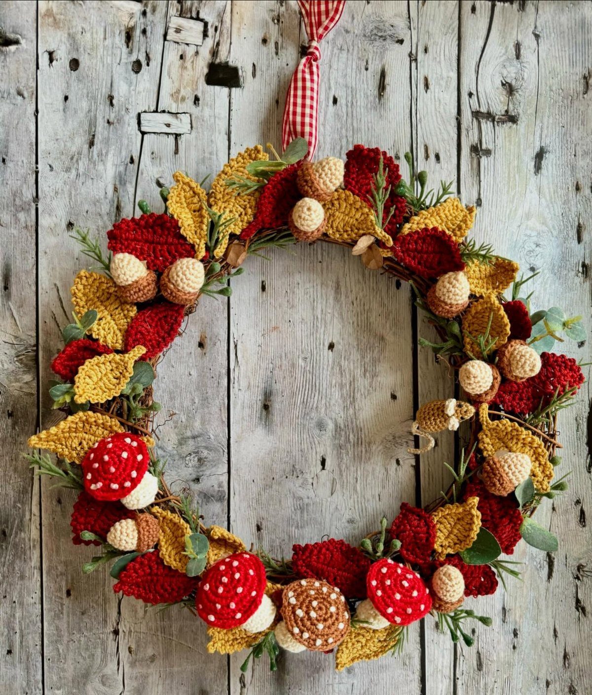 Crochet autumn wreath with red mushrooms and yellow leaves on a wooden wall
