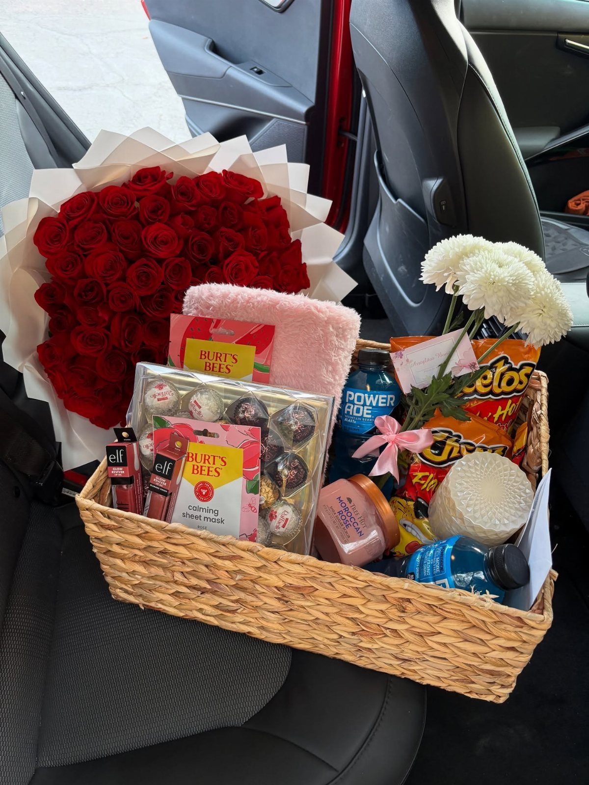 Wicker gift basket with treats and a large bouquet of red roses in a car