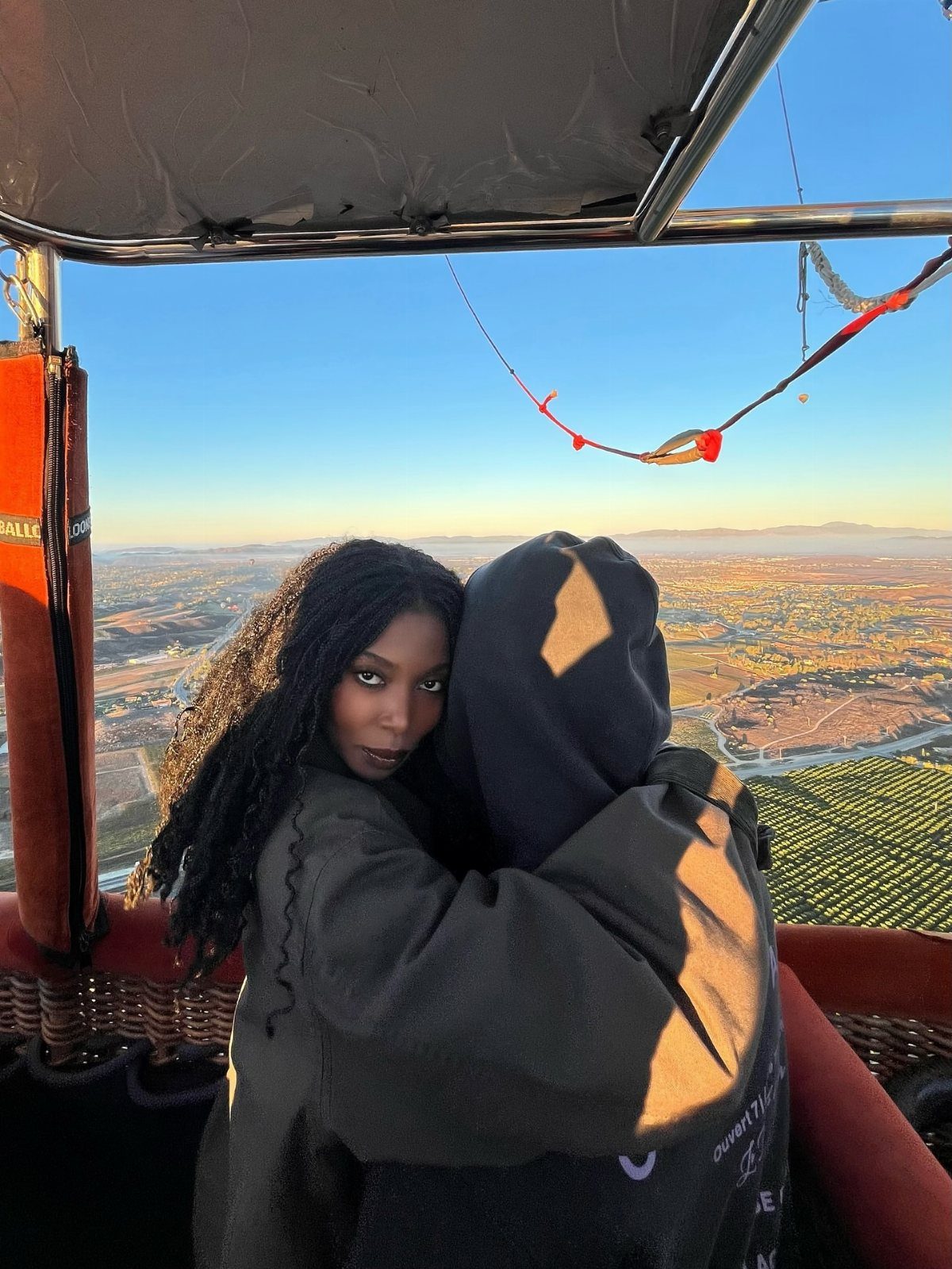 Couple hugging in a hot air balloon basket overlooking a scenic landscape at dawn.