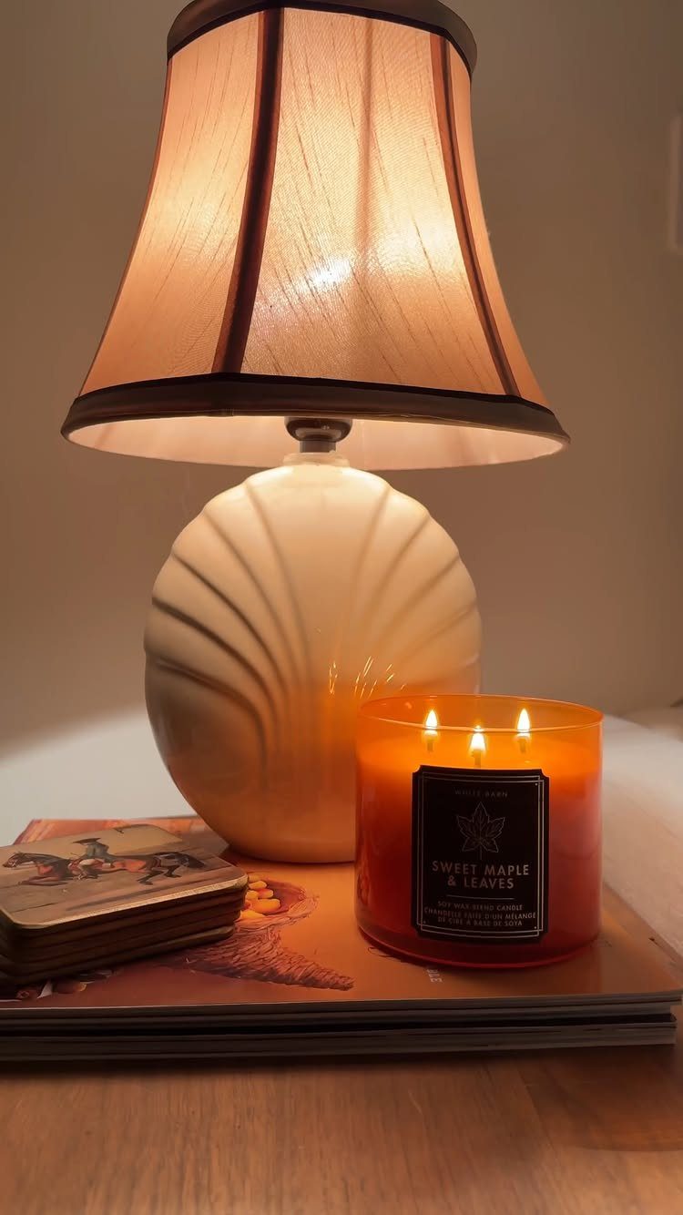 Lit orange scented candle in a glass jar next to a shell lamp.