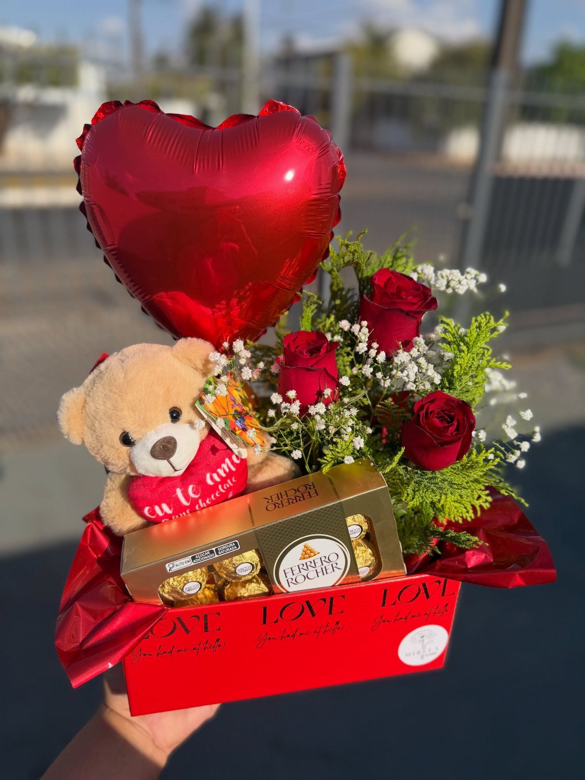 Gift box with red roses, heart balloon, teddy bear, and Ferrero Rocher chocolates.