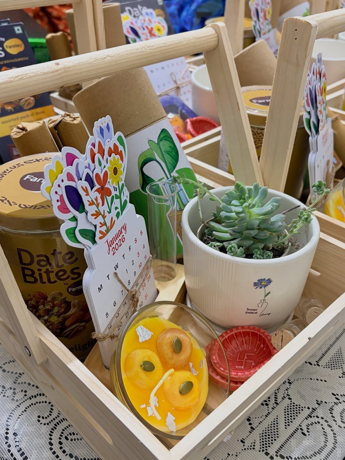 Diwali Gift Hampers: 8 Ideas for Sweets, Dry Fruit & More 5 Wooden gift hamper with date bites, a succulent plant, sweets, and a diya.