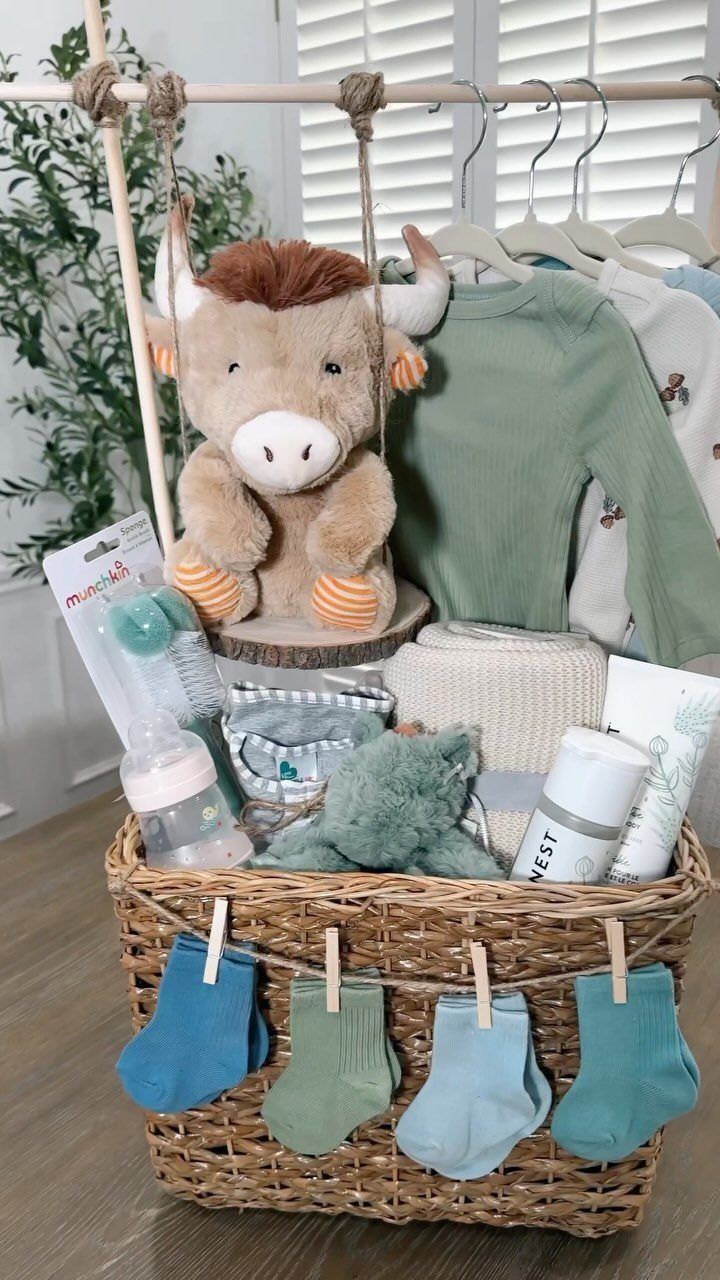 Woven gift basket filled with baby clothes, plush toys, and socks for a baby shower.