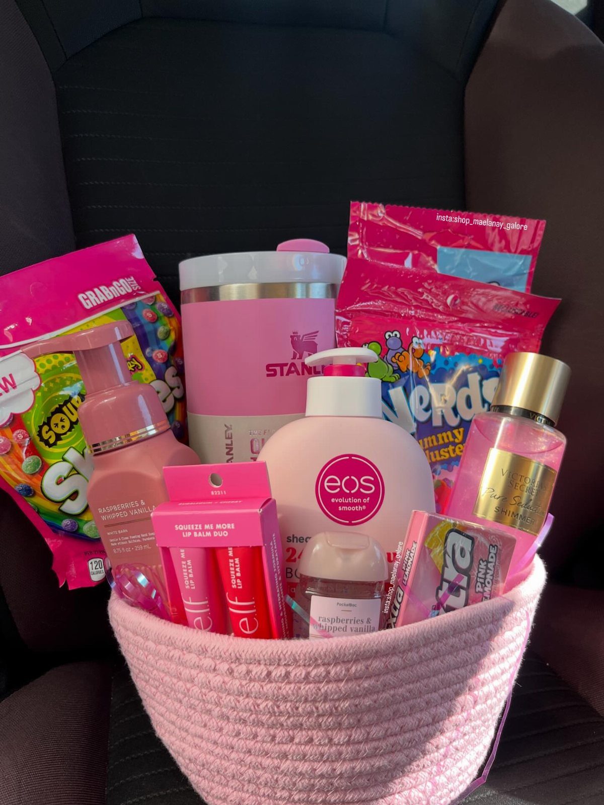 Pink woven basket filled with pink beauty products, a tumbler, and colorful candies.