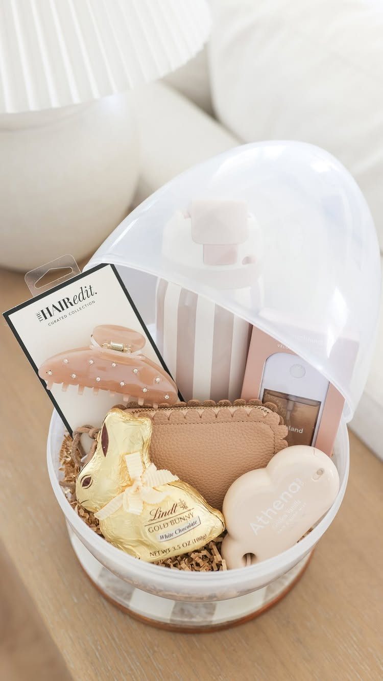 Clear egg-shaped gift basket filled with chocolates, beauty products, and a hair clip.