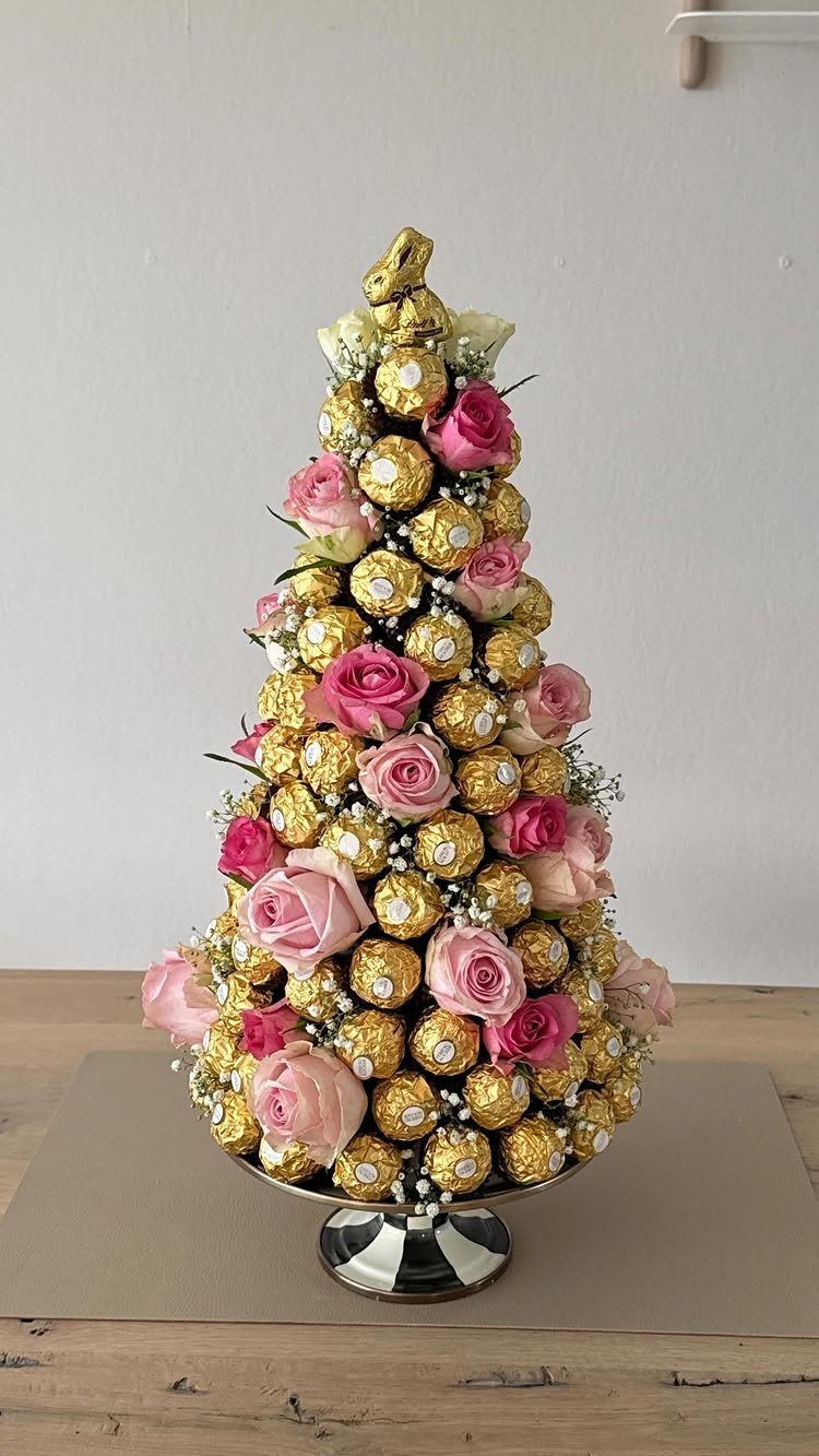 Conical chocolate tower with gold-wrapped candies and pink roses on a silver stand.