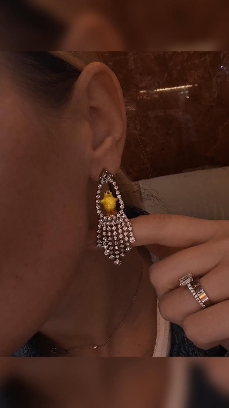 Silver dangling earring with a small yellow chick worn on a person's ear.