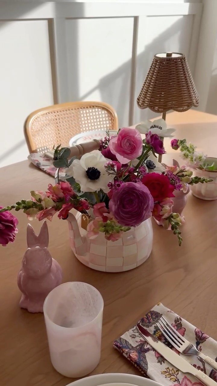 Pink and white flowers in a checkered teapot on a wooden table.