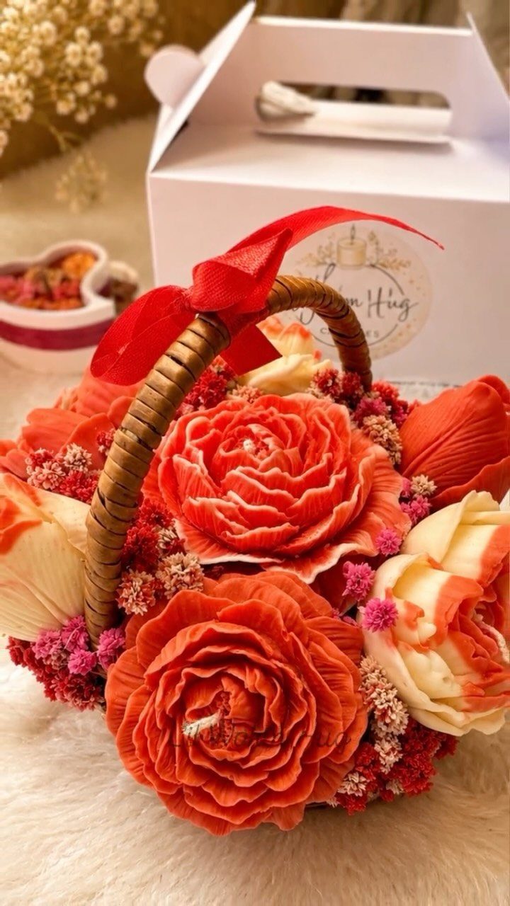 Wicker basket of orange soap flowers with a red ribbon and white gift box.
