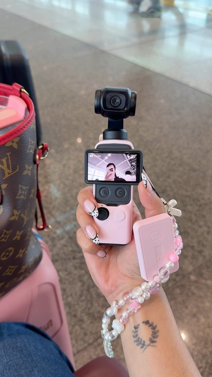 Pink compact portable camera held in a hand with a beaded wrist strap.