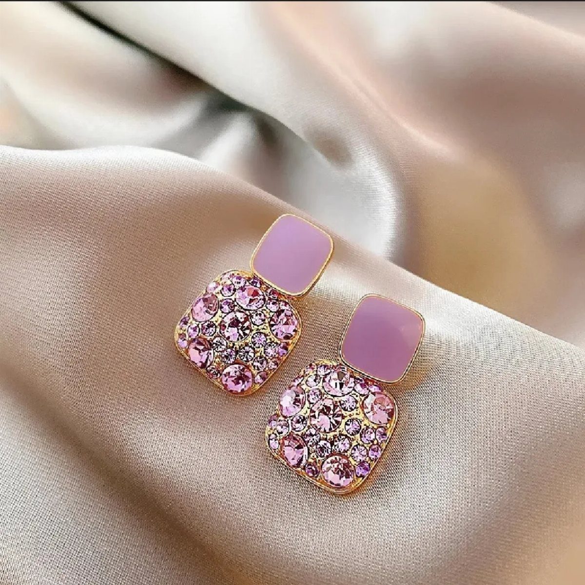 Gold square earrings with purple enamel and pink crystals on champagne satin fabric