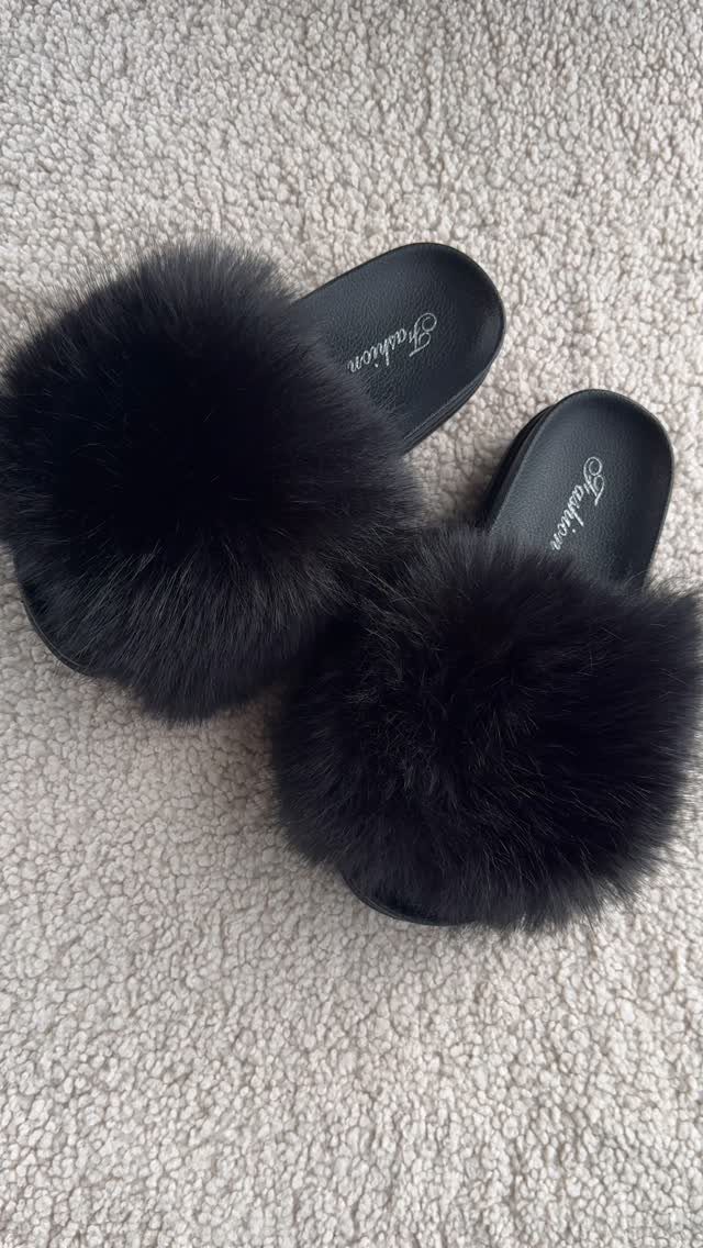 Black fluffy faux-fur slide slippers on a light grey textured carpet