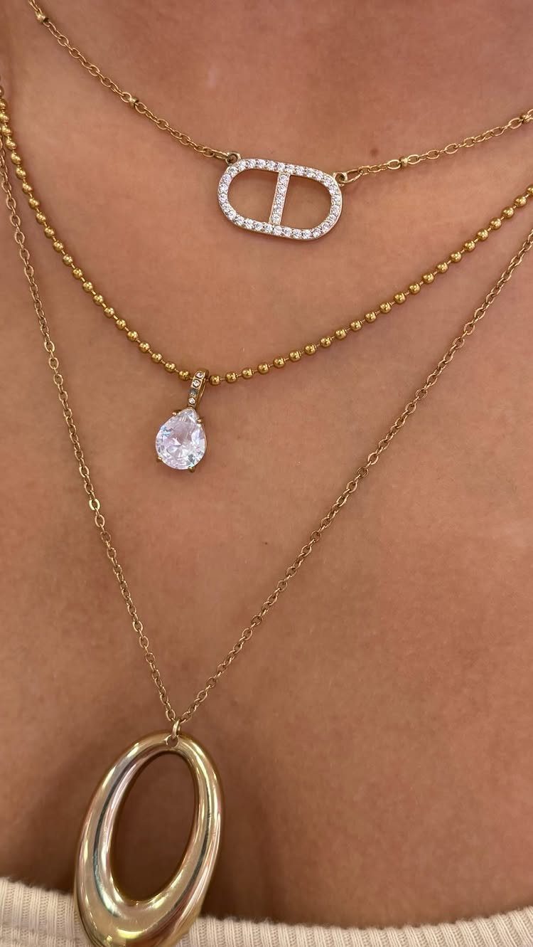 Three layered gold necklaces with crystal and oval pendants on a person's neck