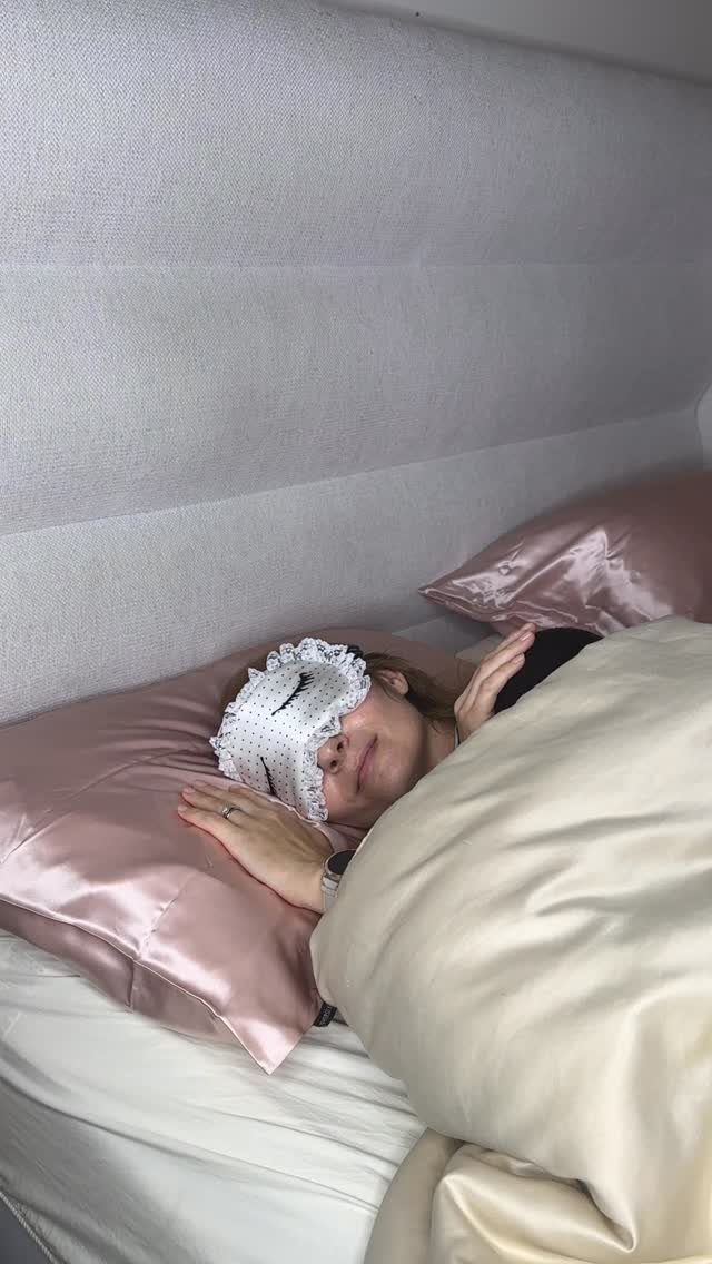 Person wearing a white lace sleep mask resting on pink satin pillows