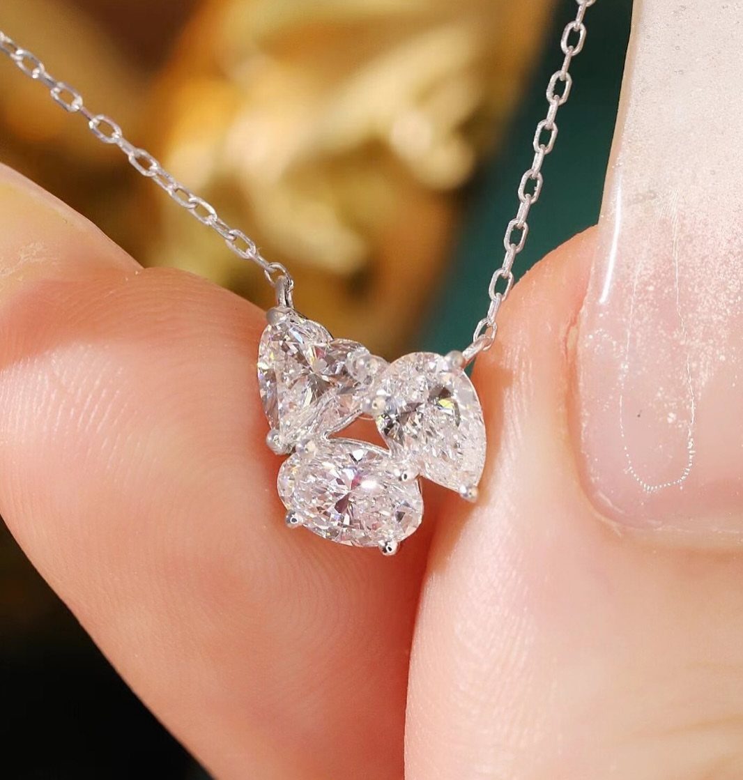 Silver necklace with three sparkling clear gemstones held by a hand with pink nails
