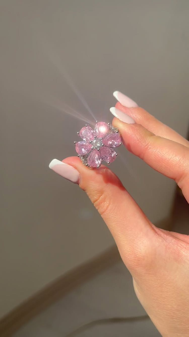 Flower-shaped ring with pink gemstones held by a hand with white nails.