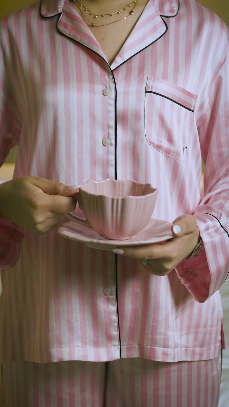 Person in pink striped satin pajamas holding a matching pink teacup and saucer