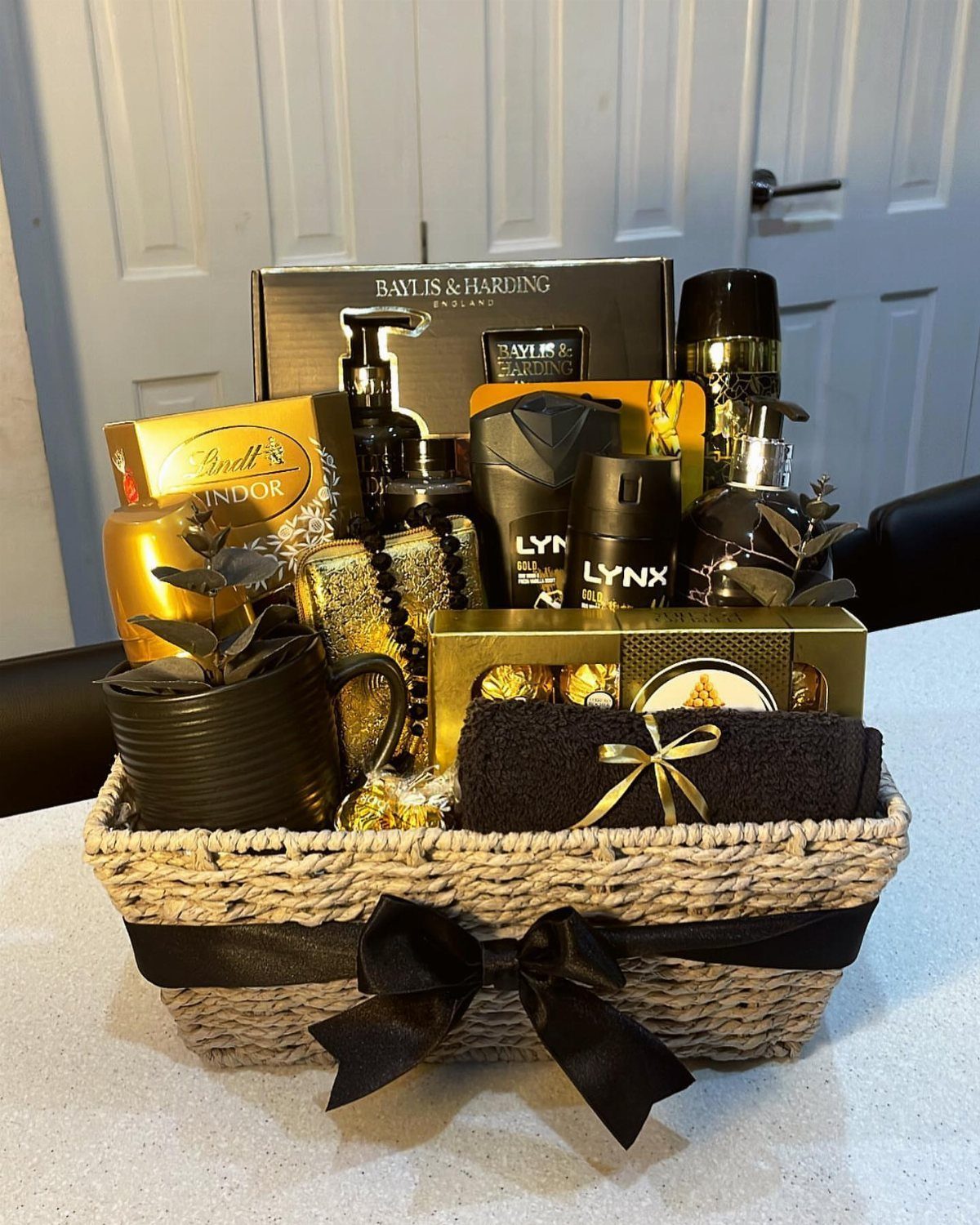 8 Fathers Day Gift Basket Ideas for Every Kind of Dad 6 Woven gift basket with black ribbon containing gold toiletries and chocolate bar.