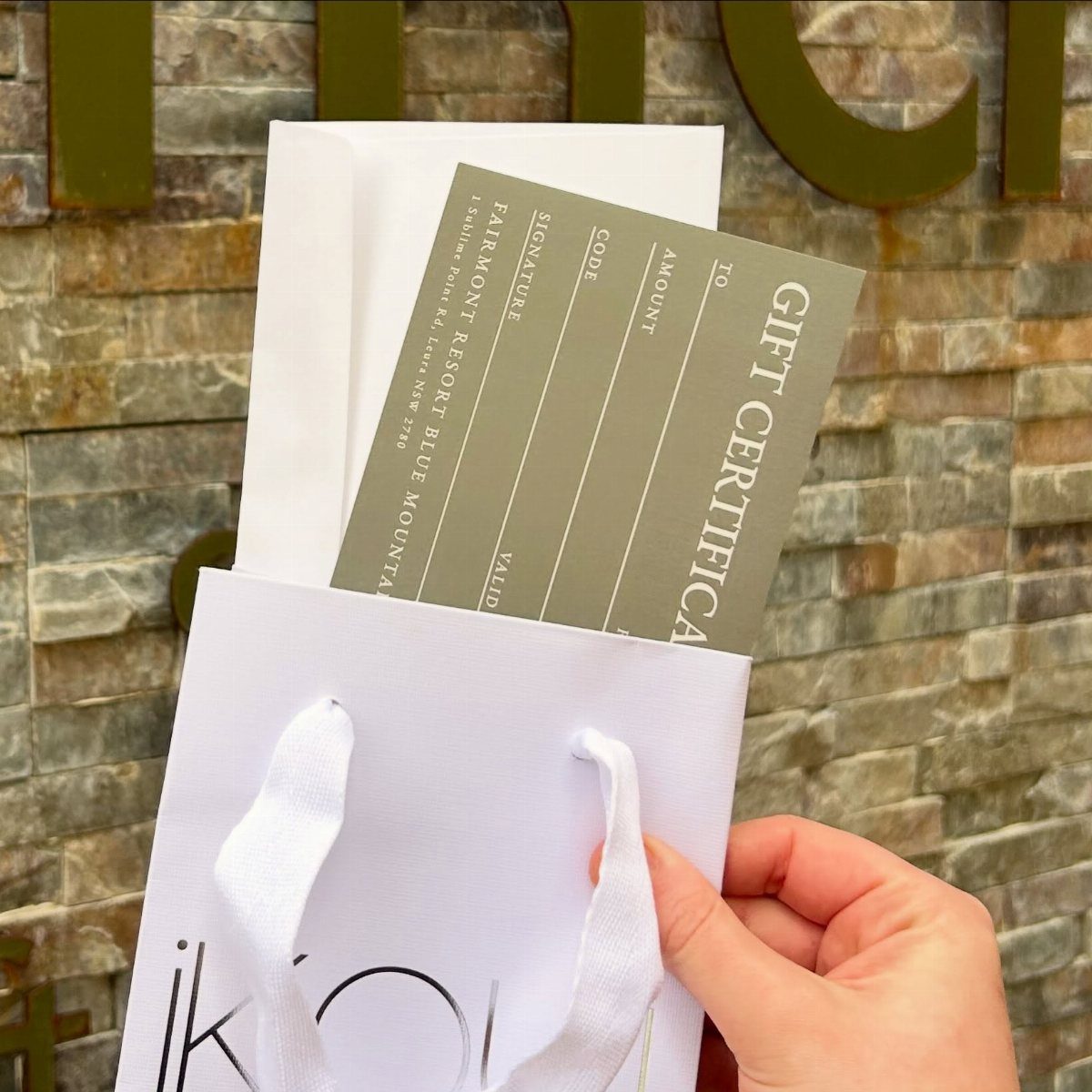 Gift certificate in a white bag held against a stone wall background