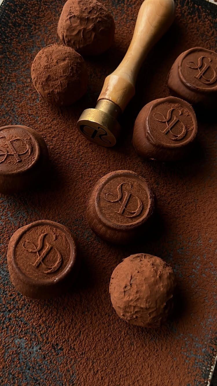 Chocolate truffles dusted in cocoa powder with a metal stamp tool on dark surface