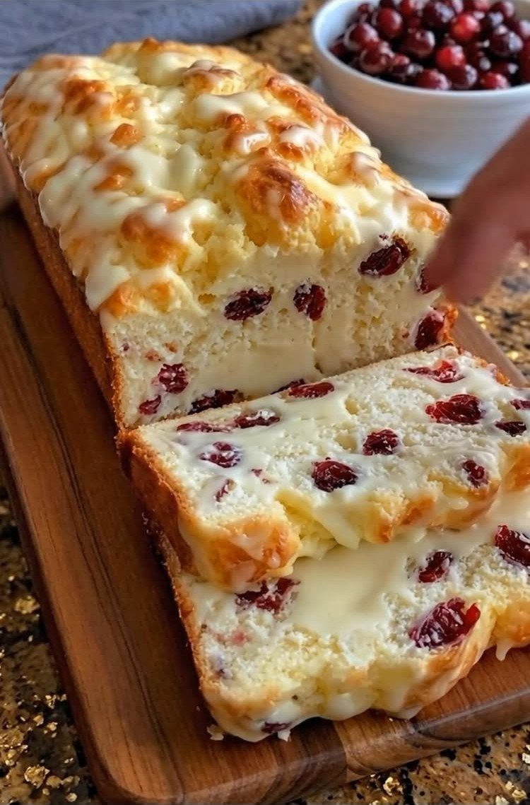Sliced cranberry bread with white glaze on a wooden board with fresh cranberries.