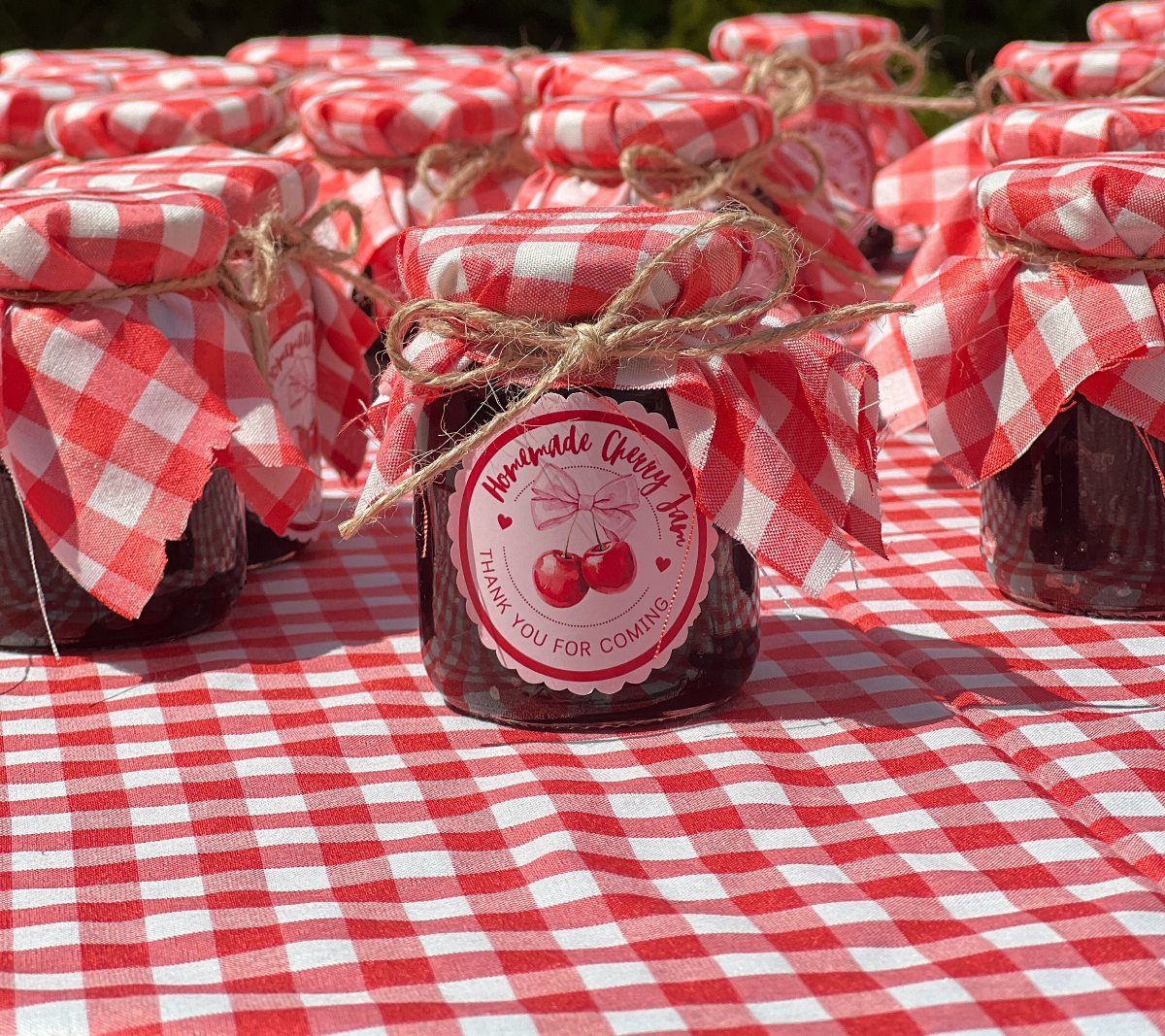 Small jars of homemade cherry jam with red checkered fabric lids on a tablecloth