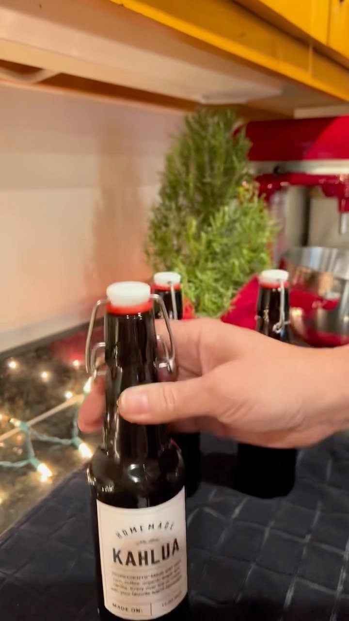 Hand holding a small bottle of homemade Kahlua coffee liqueur with festive decorations.