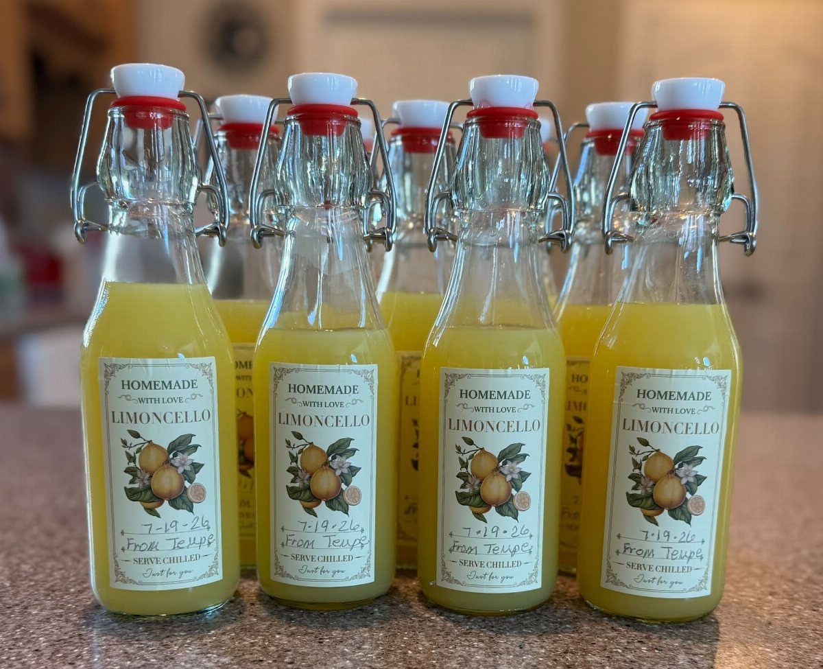 Eight glass bottles of homemade limoncello with lemon labels on a granite counter