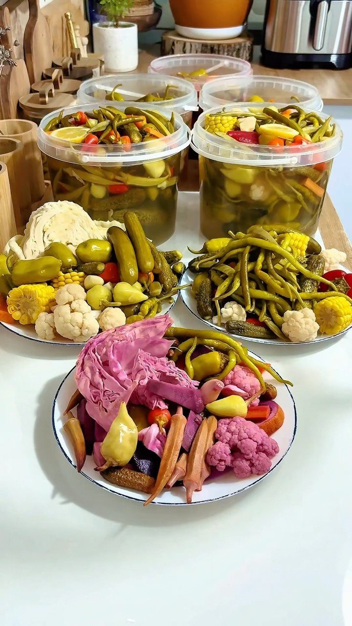 Assorted pickled vegetables in plastic containers and on plates on a white surface.